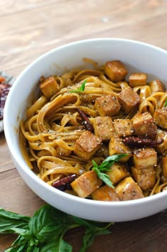 a white bowl filled with noodles and tofu on top of a wooden table next to other food items