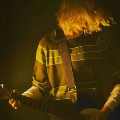 a young man playing an electric guitar in front of a dark background with light coming from behind him