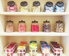 a shelf filled with lots of different types of candy in glass jars on top of white shelves