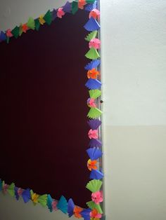 a mirror that has some colorful paper flowers on the frame and is hanging on a wall