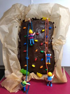 a cake with chocolate frosting and colorful decorations on it's side, being held by two small figurines