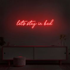 a neon sign that says let's stay in bed on the wall above a dresser