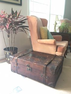 an old trunk is sitting in front of a chair with a potted plant on it