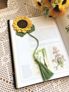 an open book with crocheted flowers and tassels on the pages, next to a bouquet of sunflowers