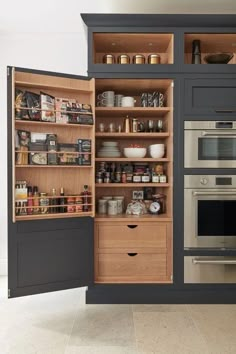 an open cabinet in the middle of a kitchen with lots of drawers and shelves filled with food