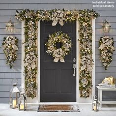 christmas wreaths are hung on the front door of a gray house with two lanterns