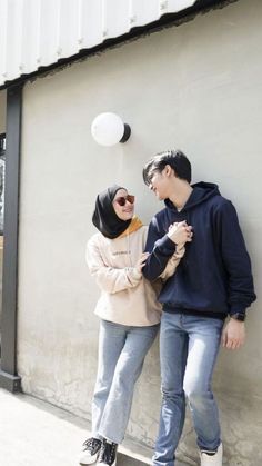 a man and woman standing next to each other near a wall with a balloon in the air