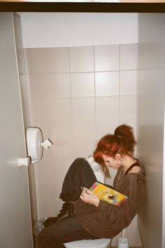 a woman sitting on the toilet reading a book