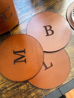 three leather coasters with the letters b, m and l on them sitting on a table