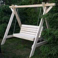 a wooden swing in the grass near some trees