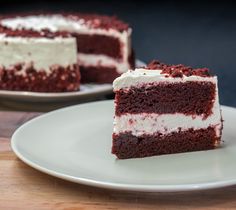 a slice of red velvet cake with white frosting sits on a plate next to the rest of the cake