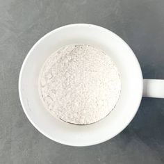 a white bowl filled with flour sitting on top of a gray counter next to a spoon