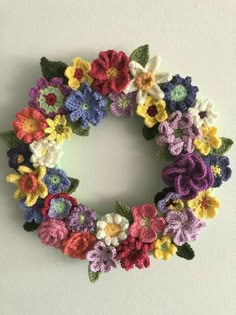 a crocheted wreath is hanging on the wall, with flowers in different colors