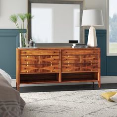 a wooden dresser sitting in front of a window next to a white lamp and large mirror