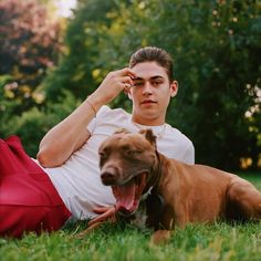 a man laying in the grass with his dog next to him and looking at the camera