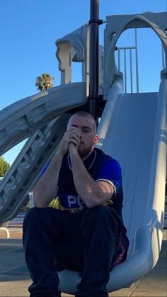 a man sitting on top of a slide in front of a playground with his hands to his face