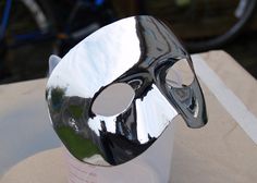 a shiny silver mask sitting on top of a white cup next to a black bicycle