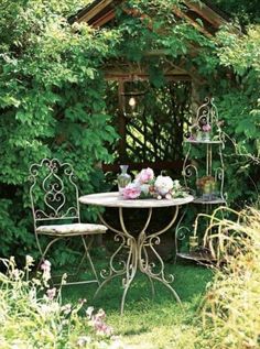 an outdoor table and chairs with flowers on it in the grass near some bushes,