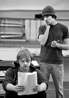 a man sitting on top of a bench next to a woman holding a paper in her hand