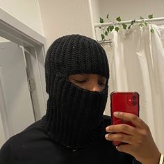 a person wearing a black ski mask holding a red cell phone in front of their face