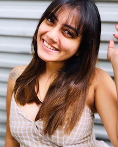 a woman with long hair smiling and holding her hand up in the air while standing next to a garage door