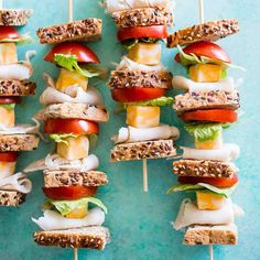 several sandwiches are arranged on toothpicks with cheese and tomatoes, lettuce and tomato slices