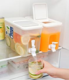 a person is holding a glass in front of an open refrigerator door with juice and water