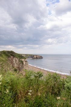 an ocean view from the top of a hill with grass growing on it and cliffs in the background