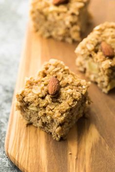 three pieces of granola sitting on top of a wooden cutting board next to nuts