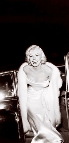 marilyn monroe sitting in the back of a car wearing a white dress and fur stole