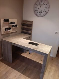 a wooden table sitting in front of a clock on the wall next to shelves with bottles