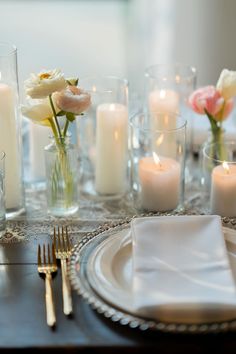 the table is set with candles and flowers in vases, napkins, and silverware