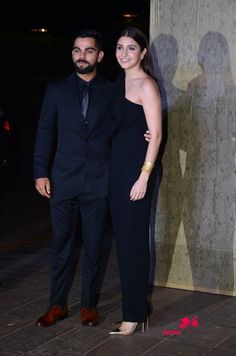 a man and woman standing next to each other in front of a wall at night