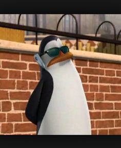 a cartoon penguin wearing sunglasses standing in front of a brick wall with a fence behind it