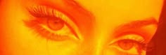 a woman's eye with long lashes and orange light shining on her face in the background