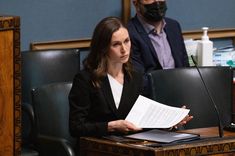 a woman sitting at a table with papers in front of her and a man standing behind her