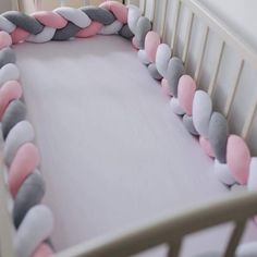 a baby crib with pink, grey and white pillows on it's sides