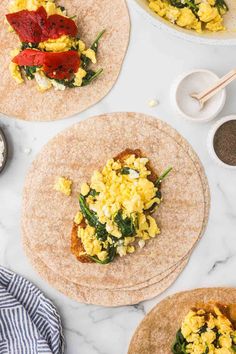 three tortillas with scrambled eggs and spinach on them, sitting on a marble countertop