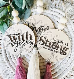 three wooden tags with tassels on top of a woven table cloth and greenery