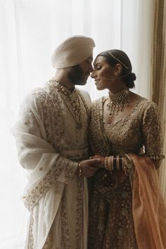 two people standing next to each other in front of a window wearing wedding outfits and jewelry