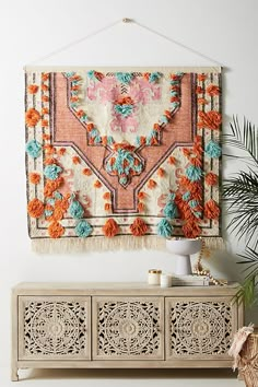 a wall hanging on the side of a white wall with an orange and blue rug