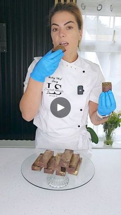 a woman in blue gloves is eating some food on a glass platter and holding a piece of chocolate