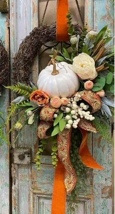 a wreath with flowers, leaves and a white pumpkin hanging on the front door for fall