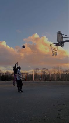 two people are playing basketball in an empty lot with the sun going down behind them