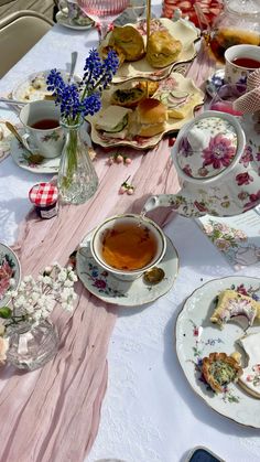 a table topped with tea cups and plates filled with food on top of a white table cloth