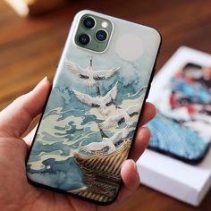 a person holding up a phone case with two birds on it and a box in the background