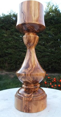 a wooden candle holder sitting on top of a white table next to trees and bushes