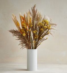 dried flowers in a white vase on a table