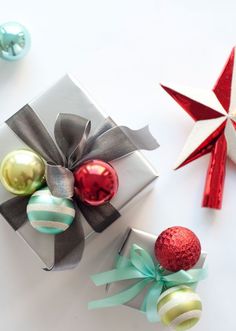 two wrapped presents with bows and ornaments next to each other on a white table top