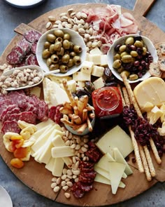 an assortment of cheeses and meats on a wooden platter with olives